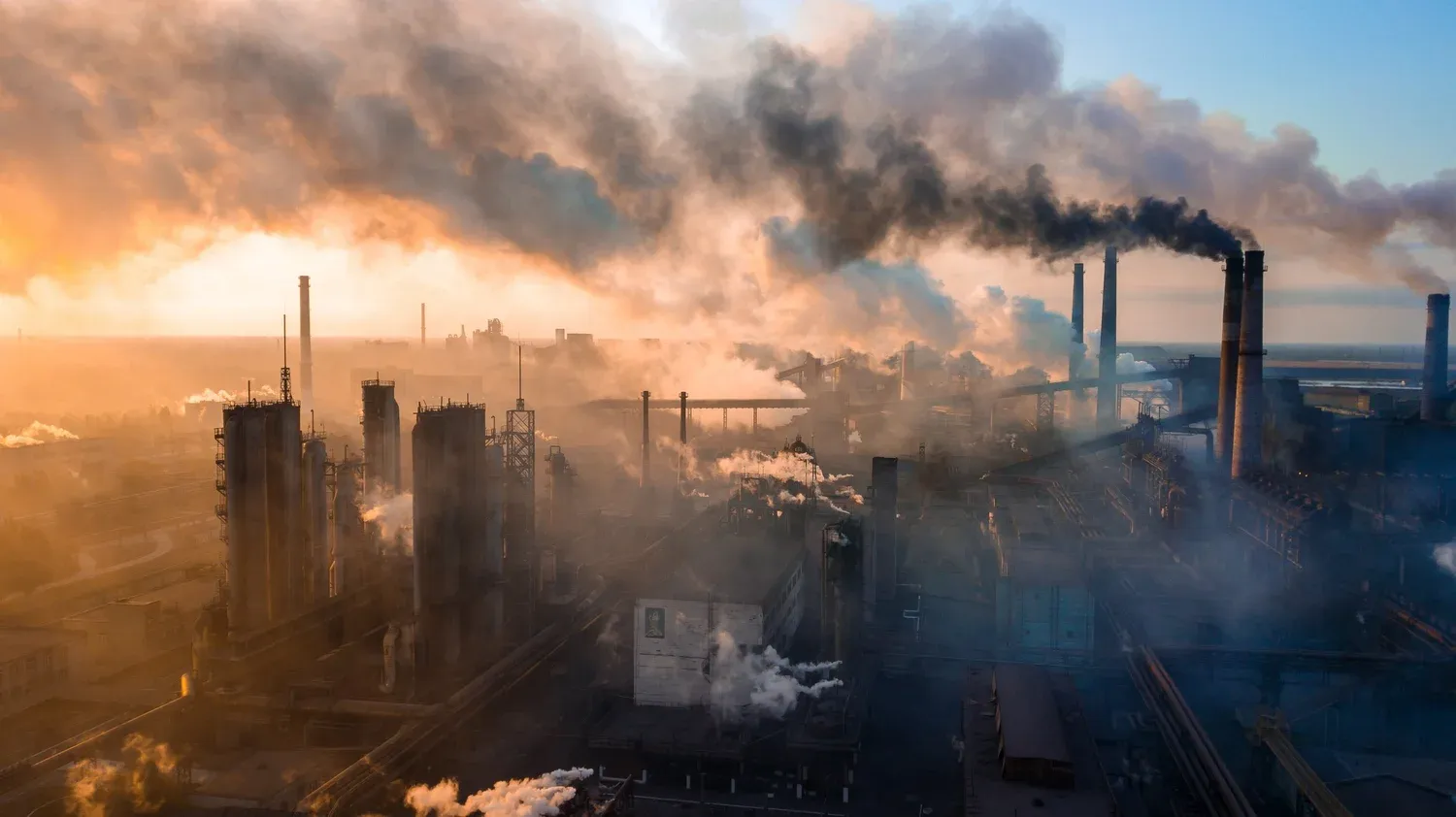 Industrial smokestacks releasing plumes of dark smoke at sunrise